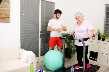 senior elderly woman with a personal trainer private fitness coach at home handsome young man