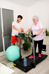 senior elderly woman with a personal trainer private fitness coach at home handsome young man