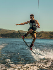 young man doing wakeboarding in a lake whit mountains also doing jumps