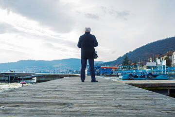 A retired man was walking alone on a wooden pontoon by the lake. The man is photographed from behind.