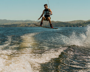 Fototapeta na wymiar young man doing wakeboarding in a lake whit mountains also doing jumps