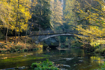 Old bridge across river Kamenice in Bohemian Switzerland, Czech Republic. Male tourist standing on a bridge and admiring beautiful autumnal calm scene