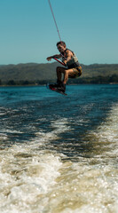 young man doing wakeboarding in a lake whit mountains also doing jumps