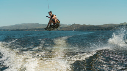 young man doing wakeboarding in a lake whit mountains also doing jumps