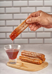 Dipping churro in raspberry sauce. Wooden board with churros