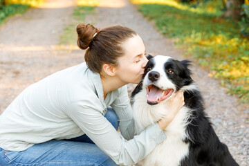 Naklejka na ściany i meble Smiling young attractive woman playing with cute puppy dog border collie on summer outdoor background. Girl holding embracing hugging dog friend. Pet care and animals concept