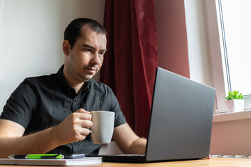 young man male sit desk, home office online notebook laptop work distance freelancer relax break hold cup