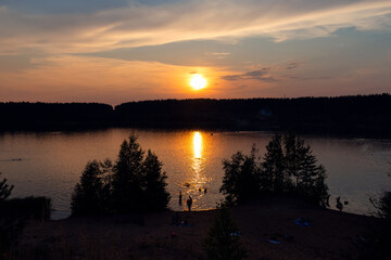 Obraz premium Evening lake with silhouettes of swimming people in reflection of sunset among the trees 