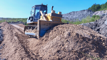 Obraz premium the process of leveling sand with a modern bulldozer during the construction of a dirt road