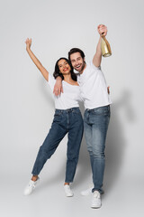 full length view of young man holding champagne bottle in raised hand near happy woman on grey.