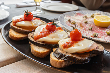 Bread toasts, with aubergine and burrata cheese, garnished with cherrie tomatoes.