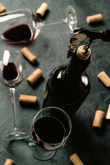 Bottle of red wine with corkscrew and glasses of wine on the background. Selective focus. Dark key photography.