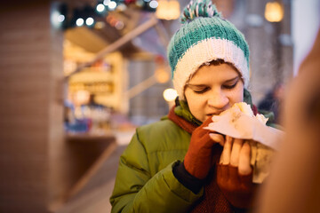 Hungry little boy eats street food at Christmas market.