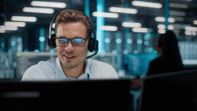 Call Center Office: Portrait of Friendly Caucasian Male Technical Customer Support Specialist Talking on a Headset, uses Computer. Client Experience Officer Helps Online via Video Conference