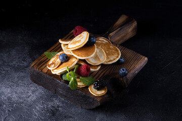 Stack of pancakes with berries on wooden board. Dark wooden background