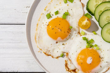 fried eggs vegetables on a white plate on a white wooden background