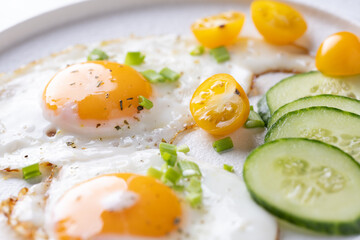 fried eggs vegetables on a white plate on a white wooden background