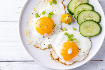 fried eggs vegetables on a white plate on a white wooden background