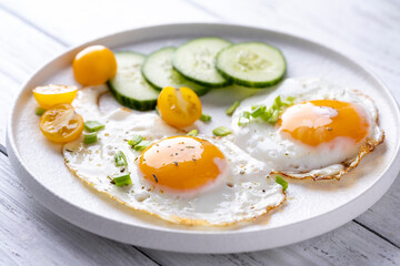 fried eggs vegetables on a white plate on a white wooden background