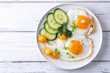 fried eggs vegetables on a white plate on a white wooden background