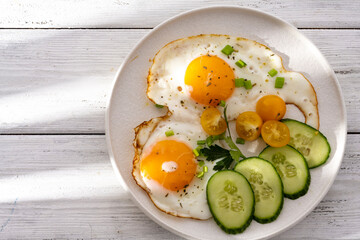 fried eggs vegetables on a white plate on a white wooden background