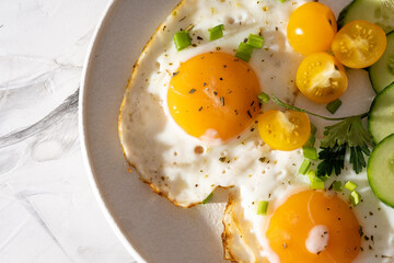 fried eggs vegetables on a white plate on a white wooden background