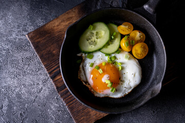 breakfast with fried eggs in a pan with bacon and vegetables on dark background
