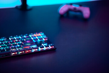 Gaming keyboard with color backlit and game controller on dark table.