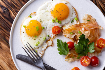 plate of fried eggs and bacon on white plate on wooden background