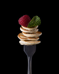 Tiny pancake with berries on a fork on a dark background
