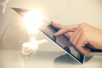Double exposure of man's hands holding and using a digital device and bulb hologram drawing. Idea concept.