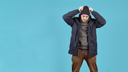 a man adjusts his hat posing in winter clothes on a blue background with a place to copy text