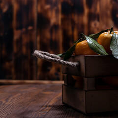 Fresh tangerines with leaves in an old box. On wooden background.
