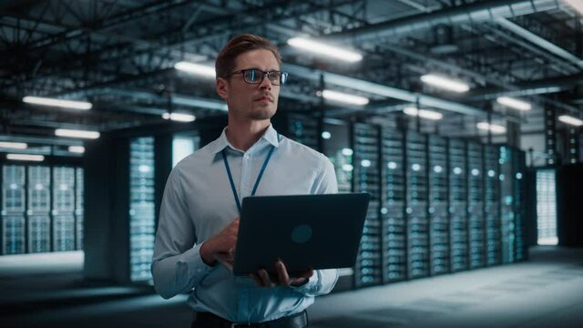 Big Data Center Chief Technology Officer Using Laptop Computer. Server Farm Cloud Computing Facility with System Administrator Working. Software as Solution and Cloud Computing with Cyber Security