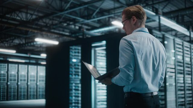 Male IT Specialist Using Tablet Computer in Data Center, Walking Through Big Data Center. Cloud Services Server, Computing Facility. Successful e-Business Digital Entrepreneur or System Administrator