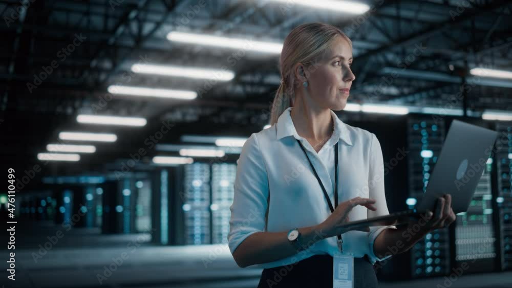 Poster successful female chief technology officer using laptop computer, standing in big warehouse data cen