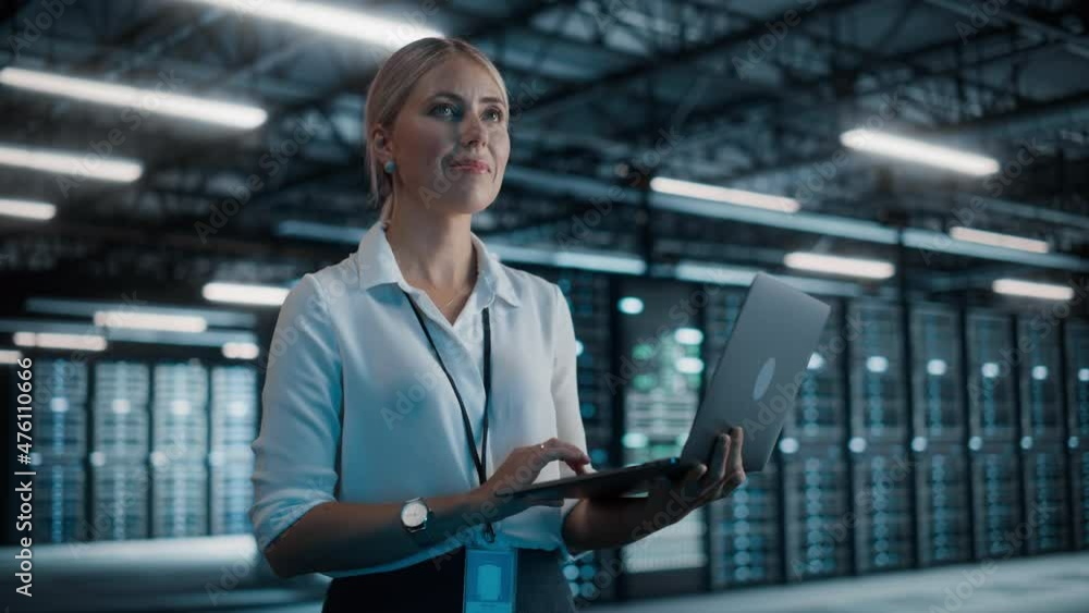 Poster successful female chief technology officer using laptop computer, standing in big warehouse data cen