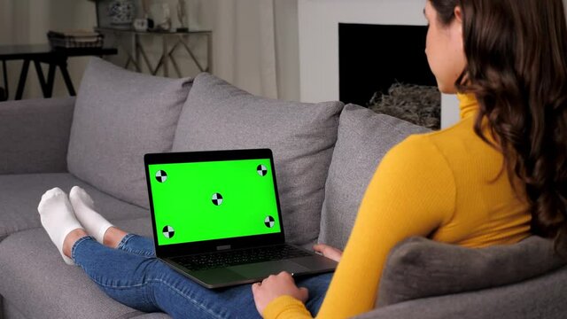 Green screen laptop woman greets talking listens online video call webcam chat. Beautiful female communicates remote connection, computer with mockup chromakey display, sitting on couch at home
