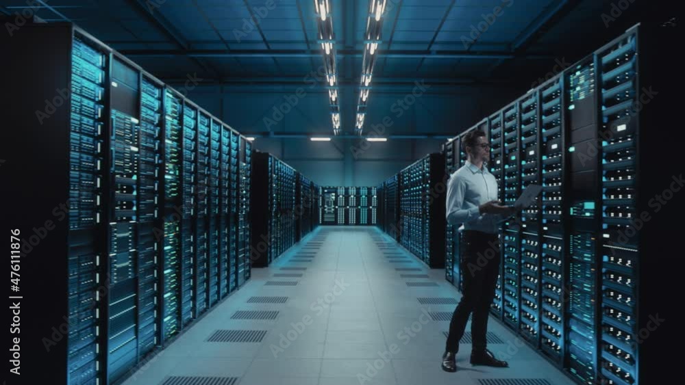 Poster Big Data Center IT Specialist Using Laptop Computer. Server Farm Cloud Computing Facility with System Administrator Working. Software as Solution, Cyber Security. Moving Between Rack Raws Dolly Shot