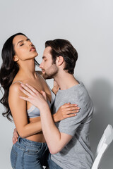 sensual brunette woman with closed eyes near man in t-shirt embracing her on grey.