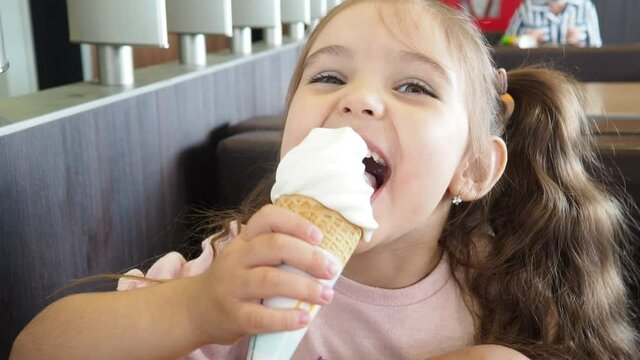 Happy surprised little girl serving ice cream .The child sits at a table in a cafe and is happy A happy childhood. cute beautiful girl eating ice cream in a cafe. sweets. family vacation. positive emo