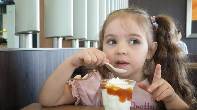 Happy surprised little girl serving ice cream .The child sits at a table in a cafe and is happy A happy childhood. cute beautiful girl eating ice cream in a cafe. sweets. family vacation. positive emo