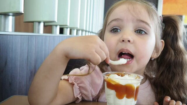 Happy surprised little girl serving ice cream .The child sits at a table in a cafe and is happy A happy childhood. cute beautiful girl eating ice cream in a cafe. sweets. family vacation. positive emo