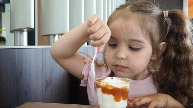 Happy surprised little girl serving ice cream .The child sits at a table in a cafe and is happy A happy childhood. cute beautiful girl eating ice cream in a cafe. sweets. family vacation. positive emo
