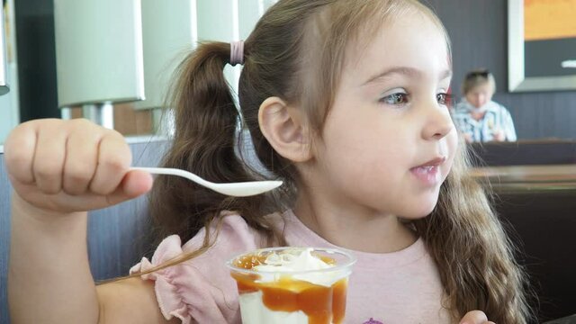 Happy surprised little girl serving ice cream .The child sits at a table in a cafe and is happy A happy childhood. cute beautiful girl eating ice cream in a cafe. sweets. family vacation. positive emo