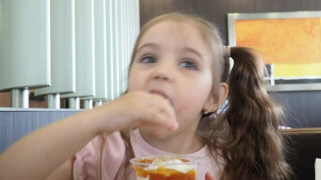 Happy surprised little girl serving ice cream .The child sits at a table in a cafe and is happy A happy childhood. cute beautiful girl eating ice cream in a cafe. sweets. family vacation. positive emo