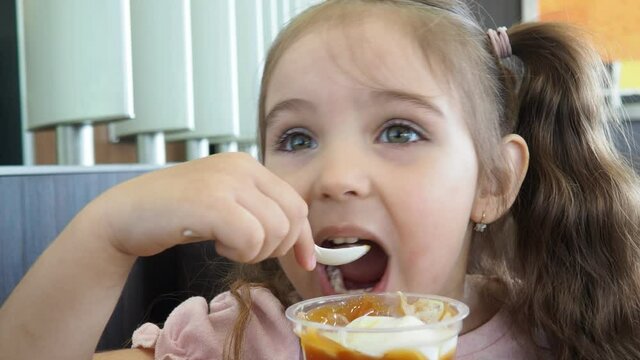 Happy surprised little girl serving ice cream .The child sits at a table in a cafe and is happy A happy childhood. cute beautiful girl eating ice cream in a cafe. sweets. family vacation. positive emo