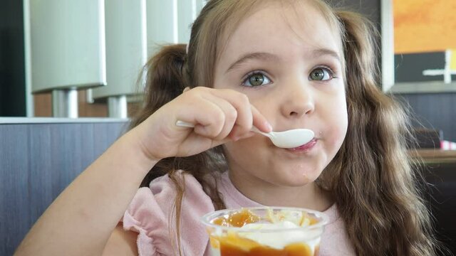 Happy surprised little girl serving ice cream .The child sits at a table in a cafe and is happy A happy childhood. cute beautiful girl eating ice cream in a cafe. sweets. family vacation. positive emo