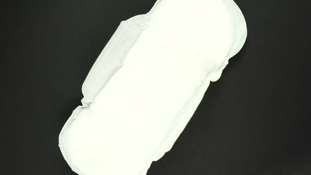 White Menstruation and sanitary napkin pad is rotating on black background. Feminine hygiene product