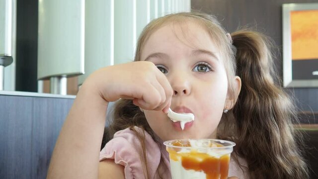 Happy surprised little girl serving ice cream .The child sits at a table in a cafe and is happy A happy childhood. cute beautiful girl eating ice cream in a cafe. sweets. family vacation. positive emo
